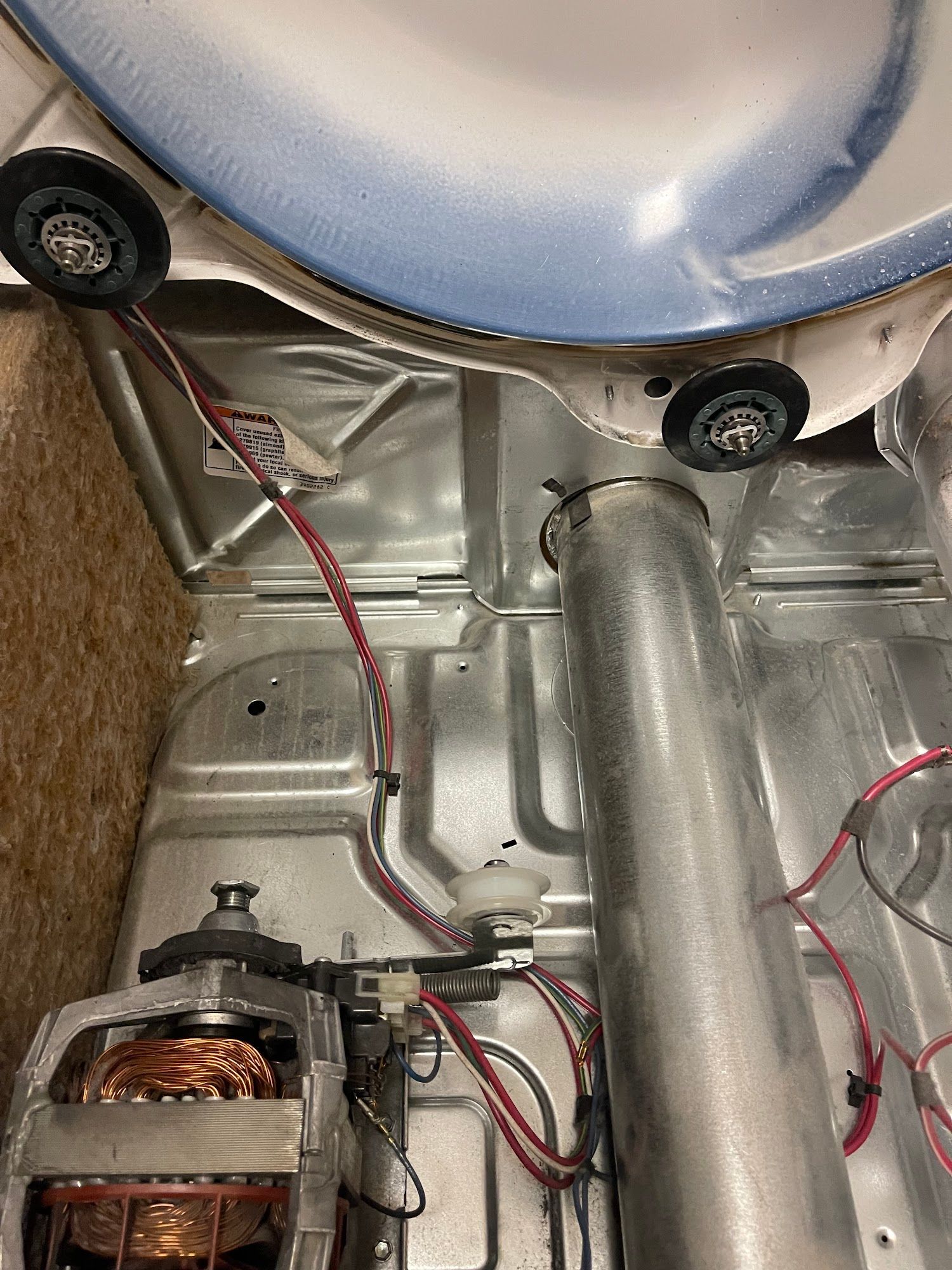 Inside of a dryer, showing the drum, rollers, motor, and vent tube.