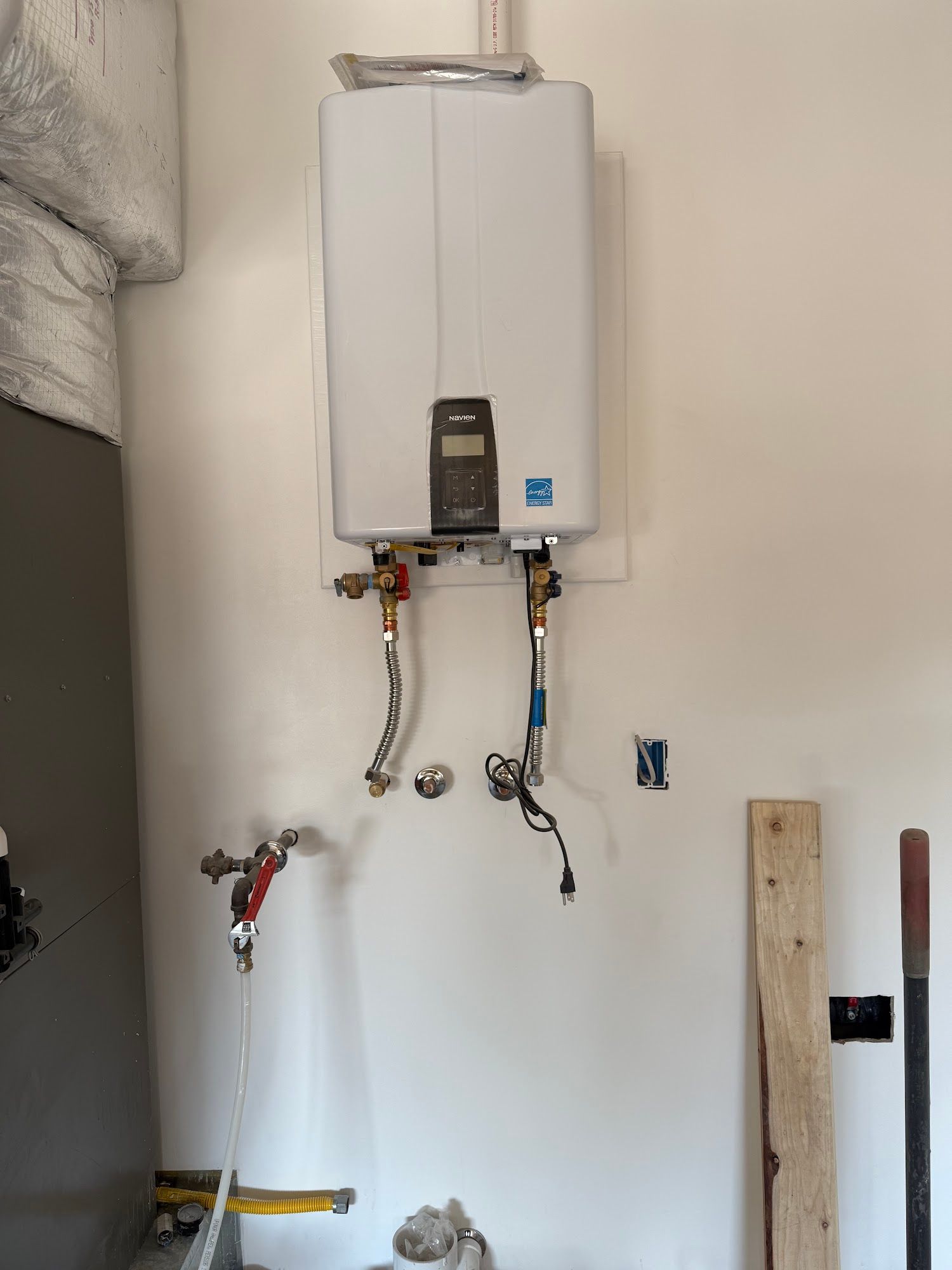White tankless water heater mounted on a white wall. Two curved pipes connect to the bottom.