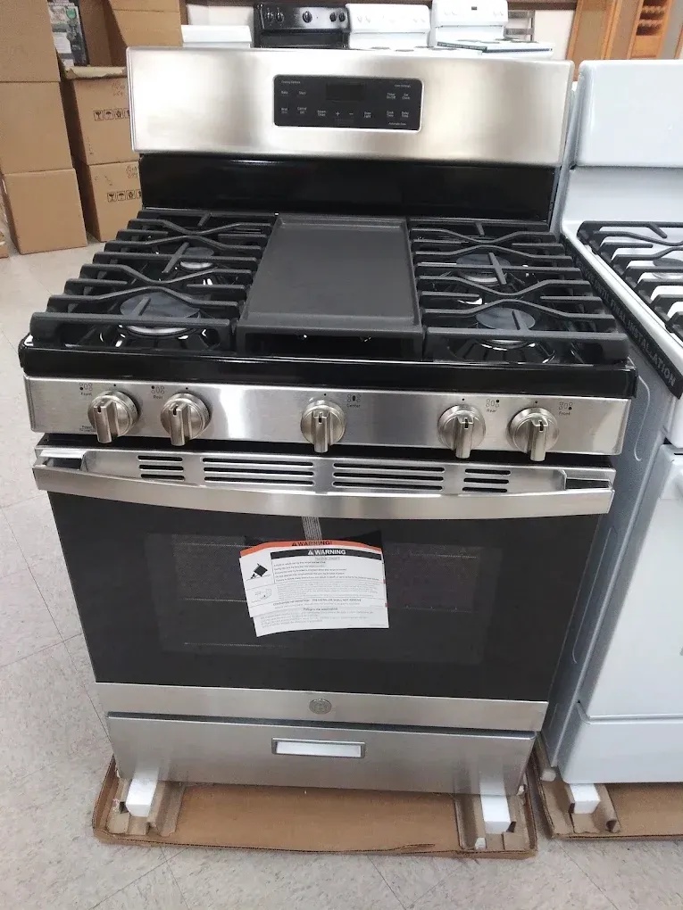 A stainless steel GE gas range with a griddle on the stovetop, in a store.