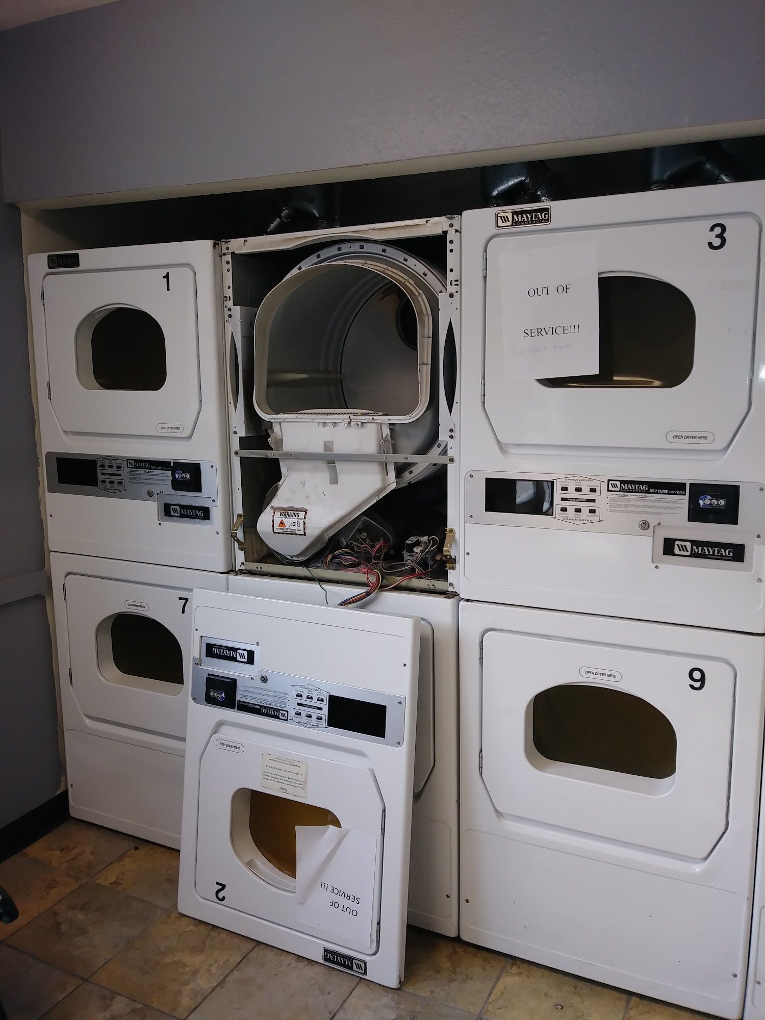 Laundry room with several white dryers, one disassembled.