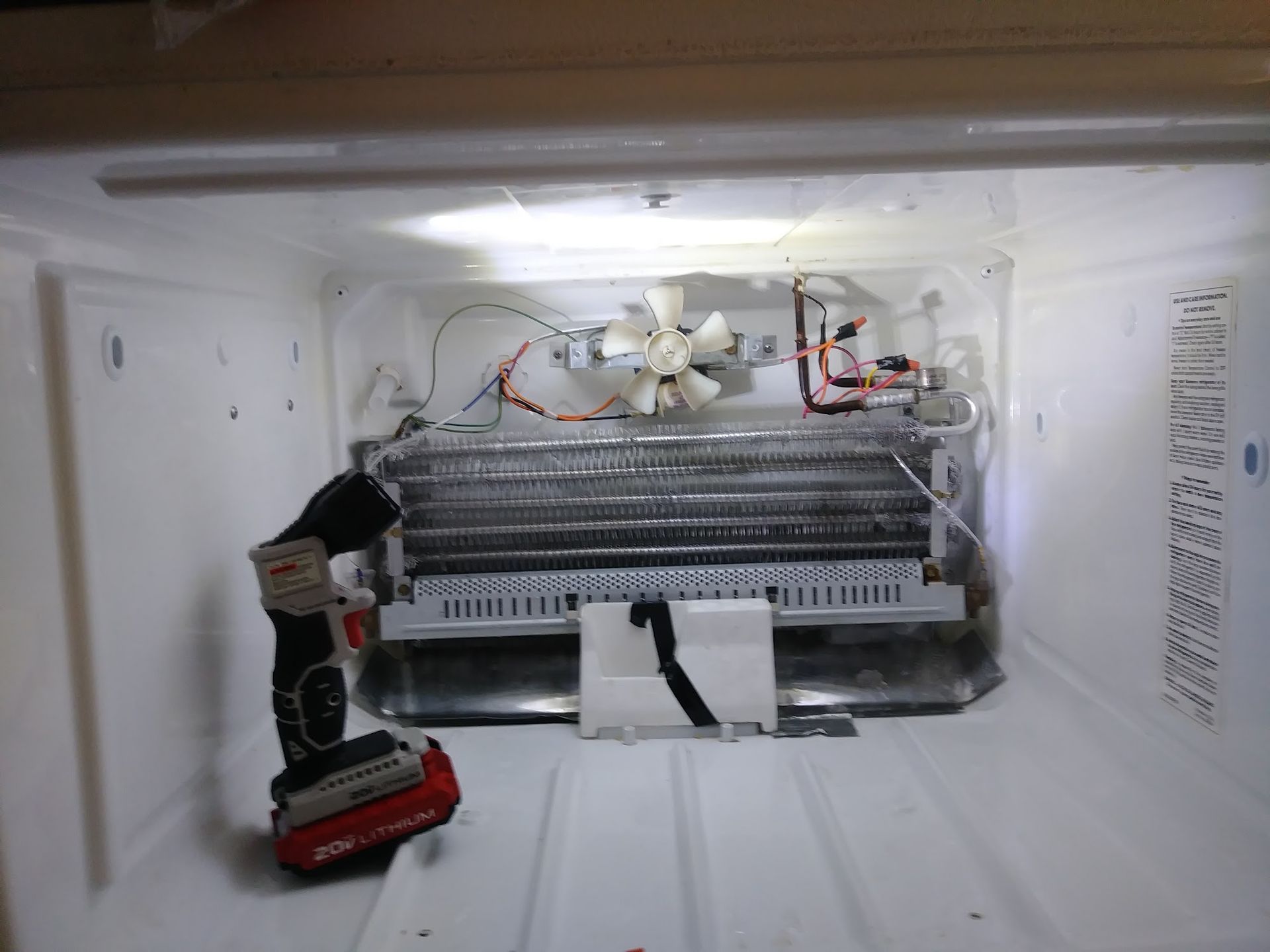 Refrigerator interior; exposed coils with ice, a fan, and a power drill.