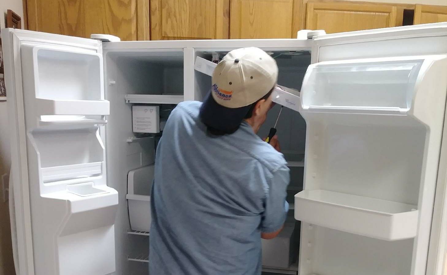 A man repairing a white refrigerator in a kitchen.