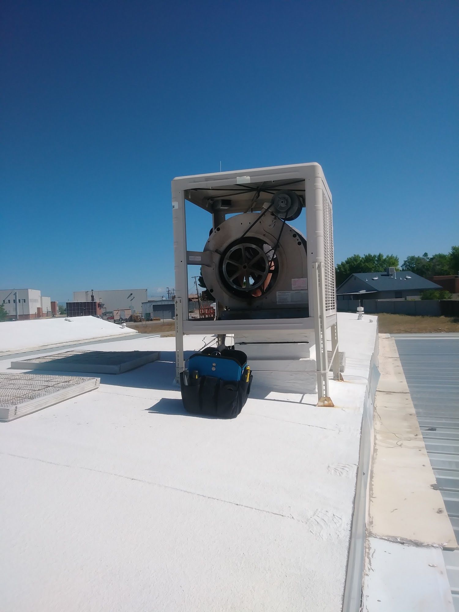 HVAC unit on a white roof, with a blue sky. A black toolbox sits nearby.