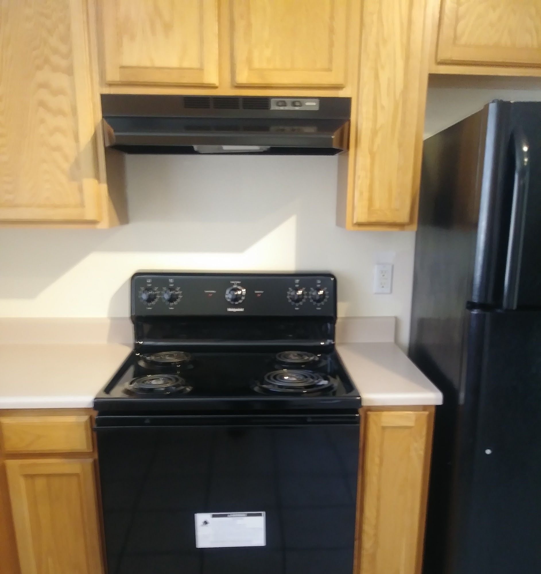 Kitchen with black stove and refrigerator, tan cabinets, and white countertops.