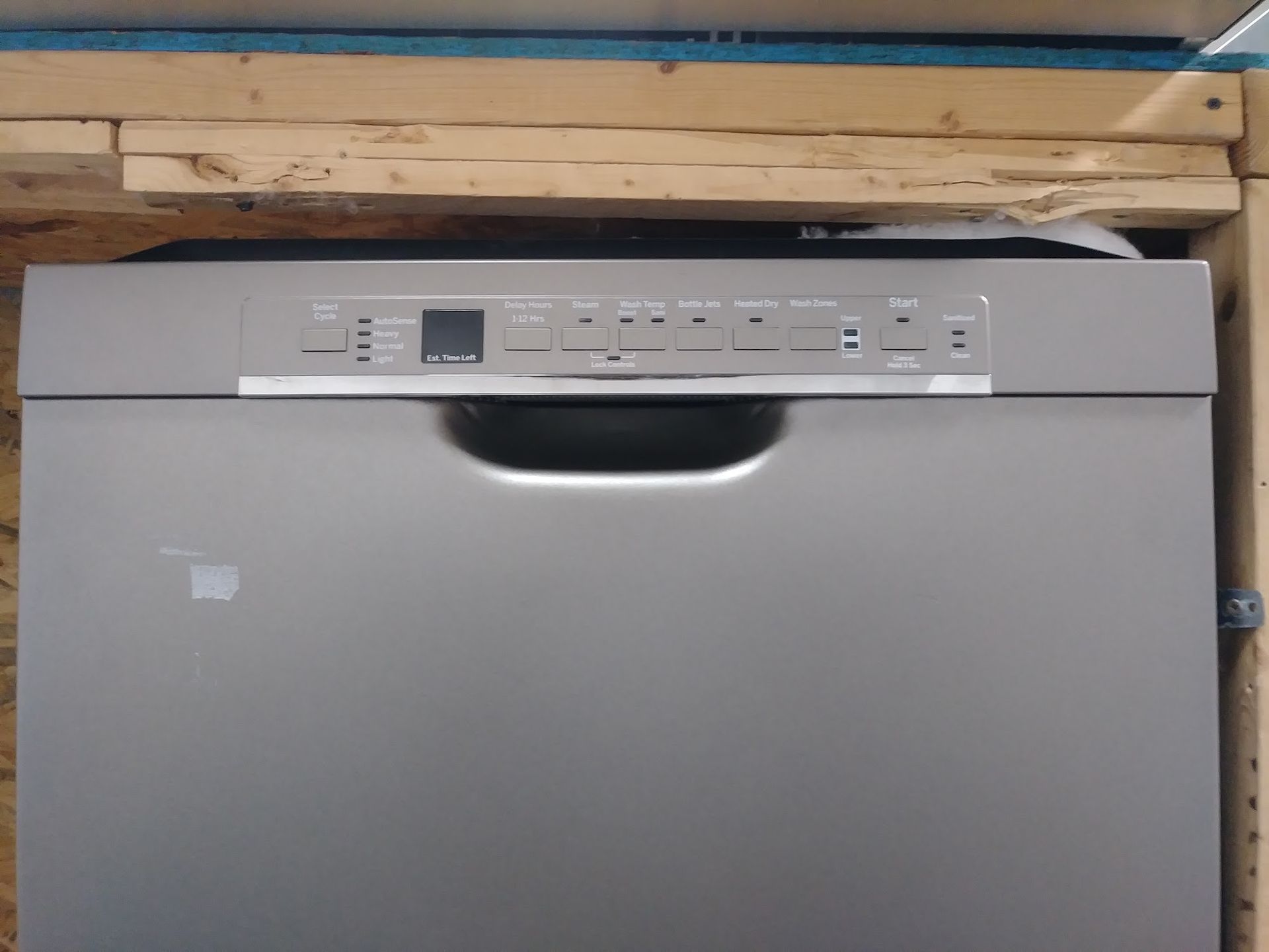 A silver dishwasher with an embedded control panel, set in a wooden cabinet.