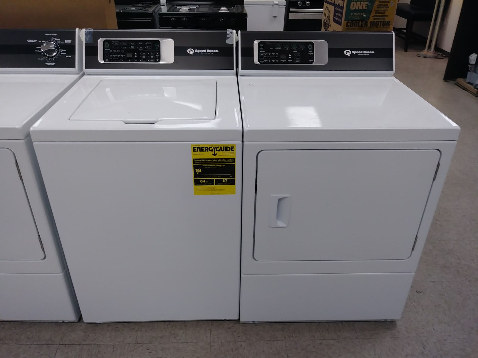 White washing machine and dryer set with black control panels, in a store setting.