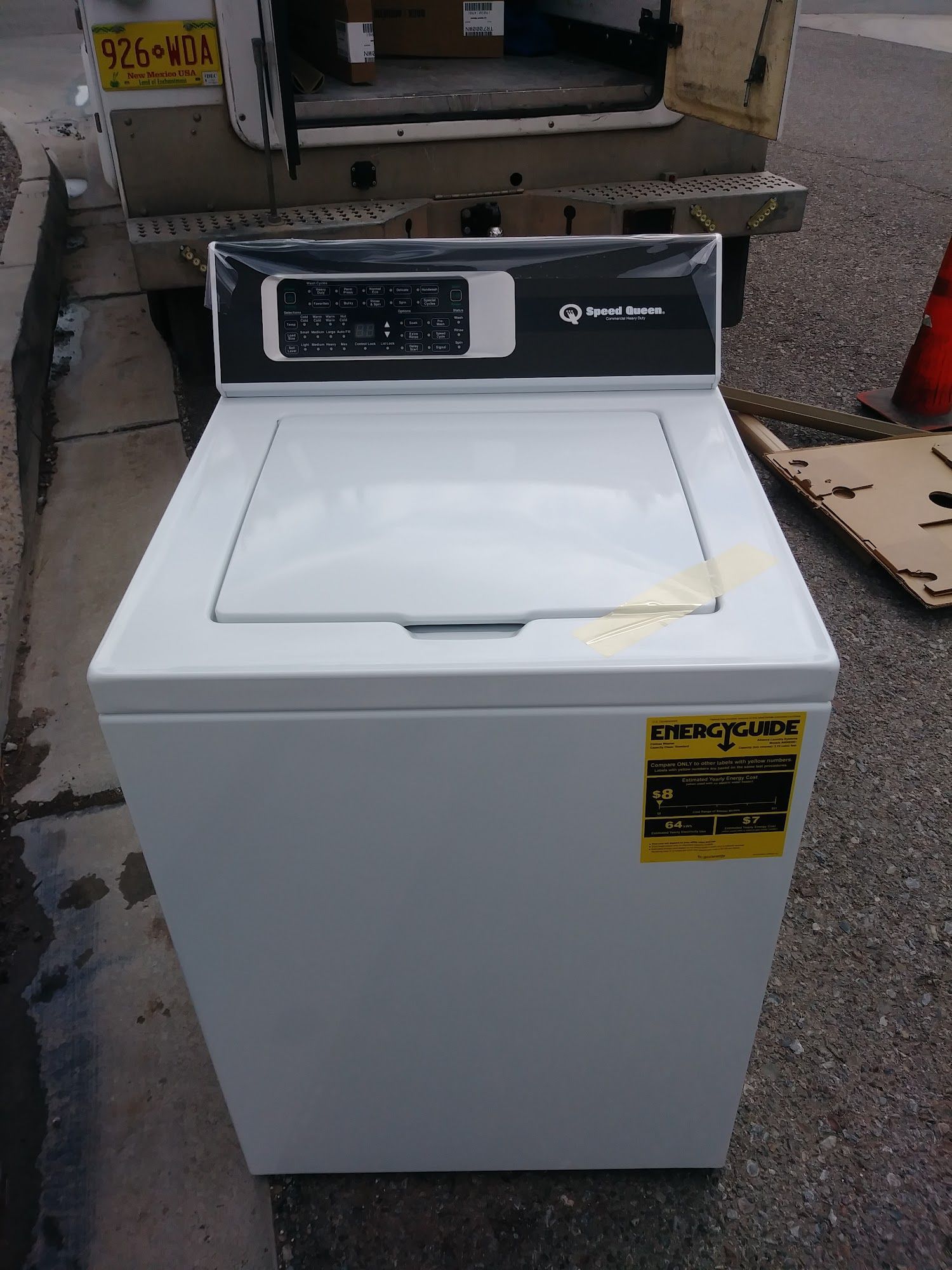 White Speed Queen top-load washing machine, on a sidewalk, near a van.