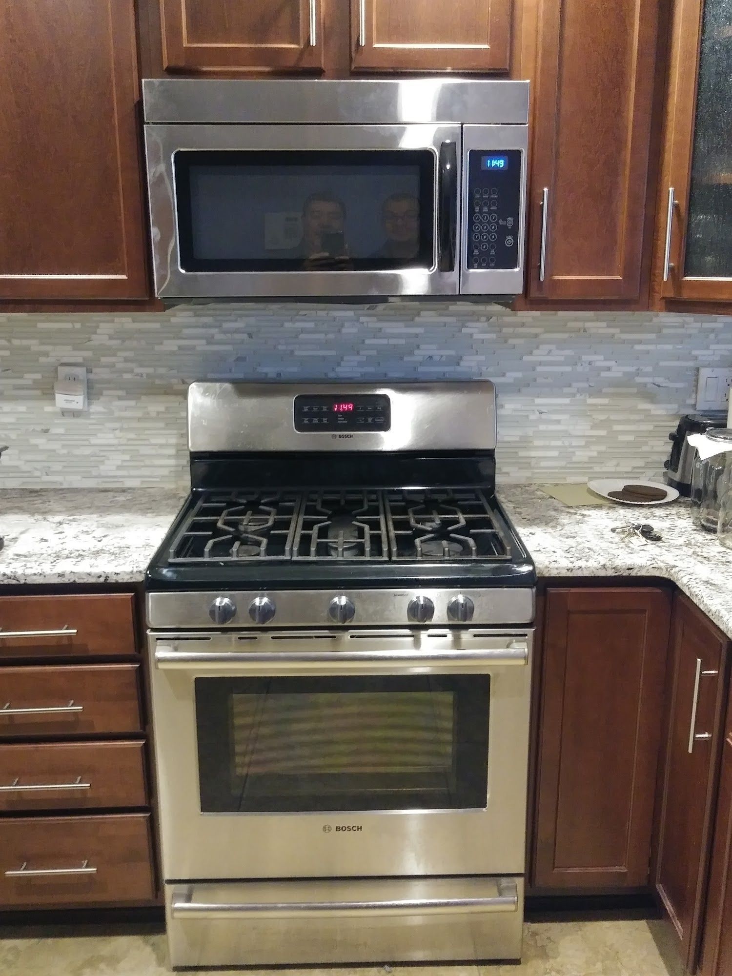 Stainless steel gas range and microwave oven installed in a kitchen with dark cabinets.