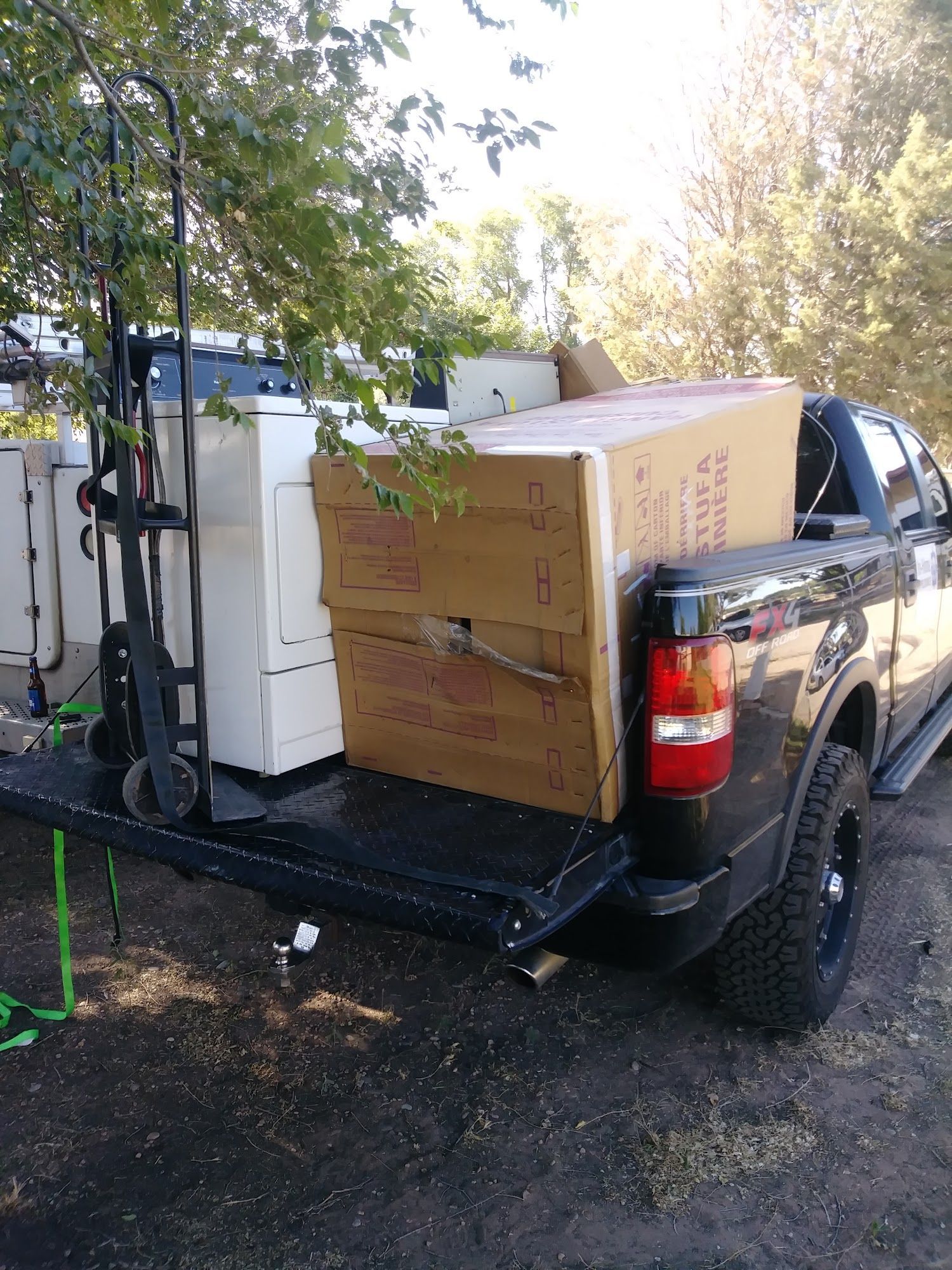 Black pickup truck loaded with appliances and boxes. A hand truck is also present.