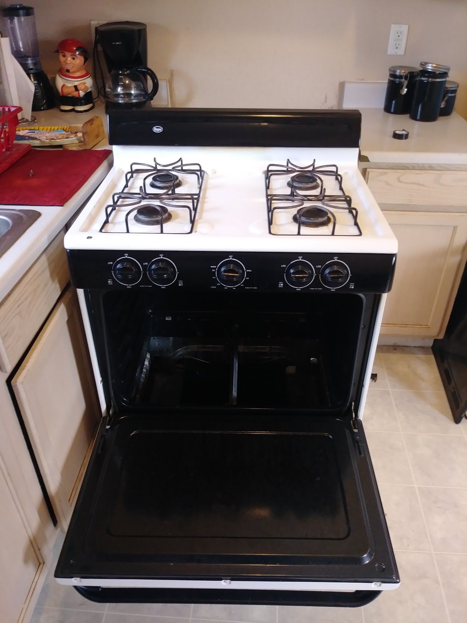 Black and white gas stove with open oven door; four burners visible.