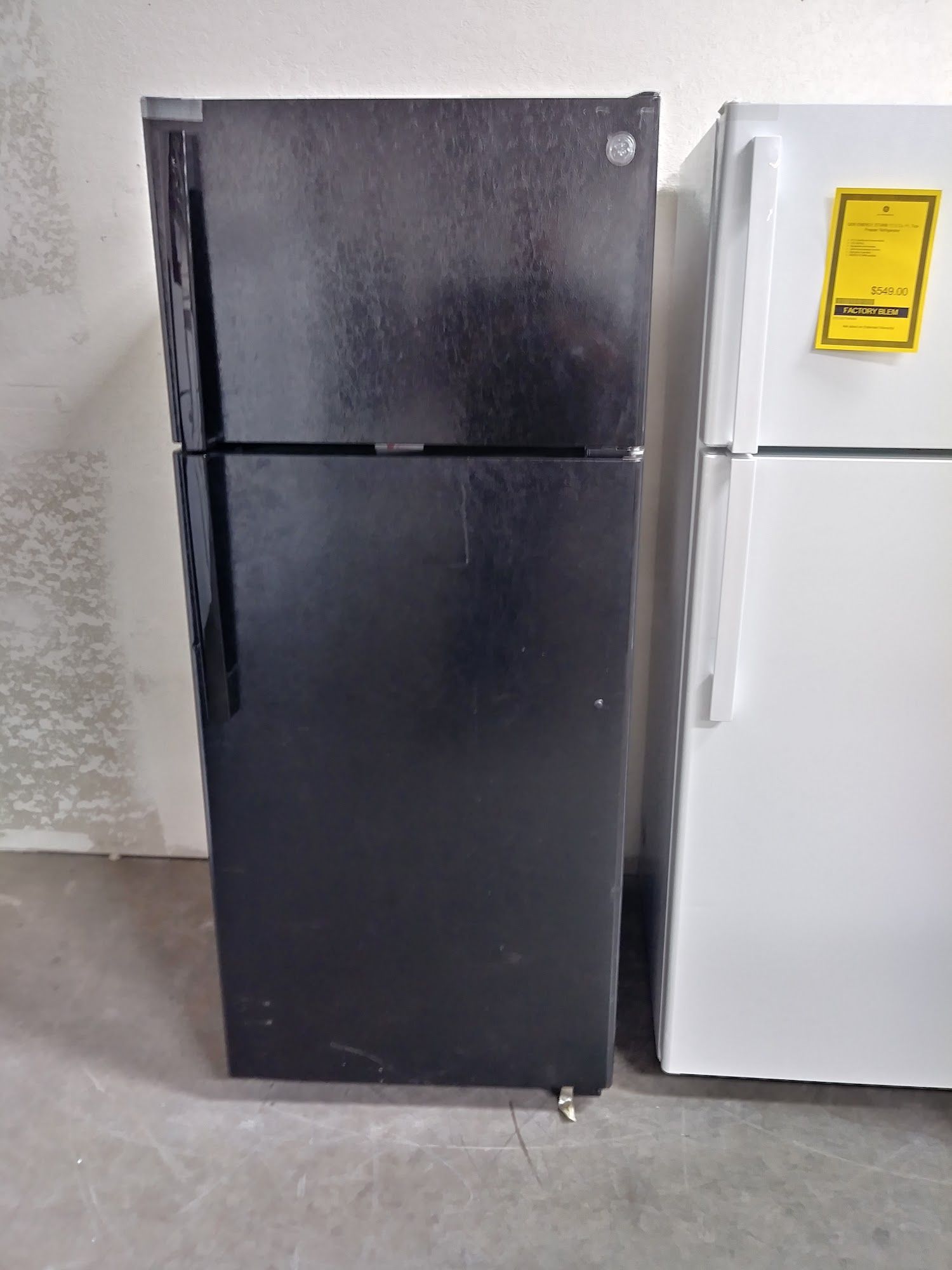 Black and white refrigerators side-by-side in a room. One is black, the other is white with a yellow energy sticker.