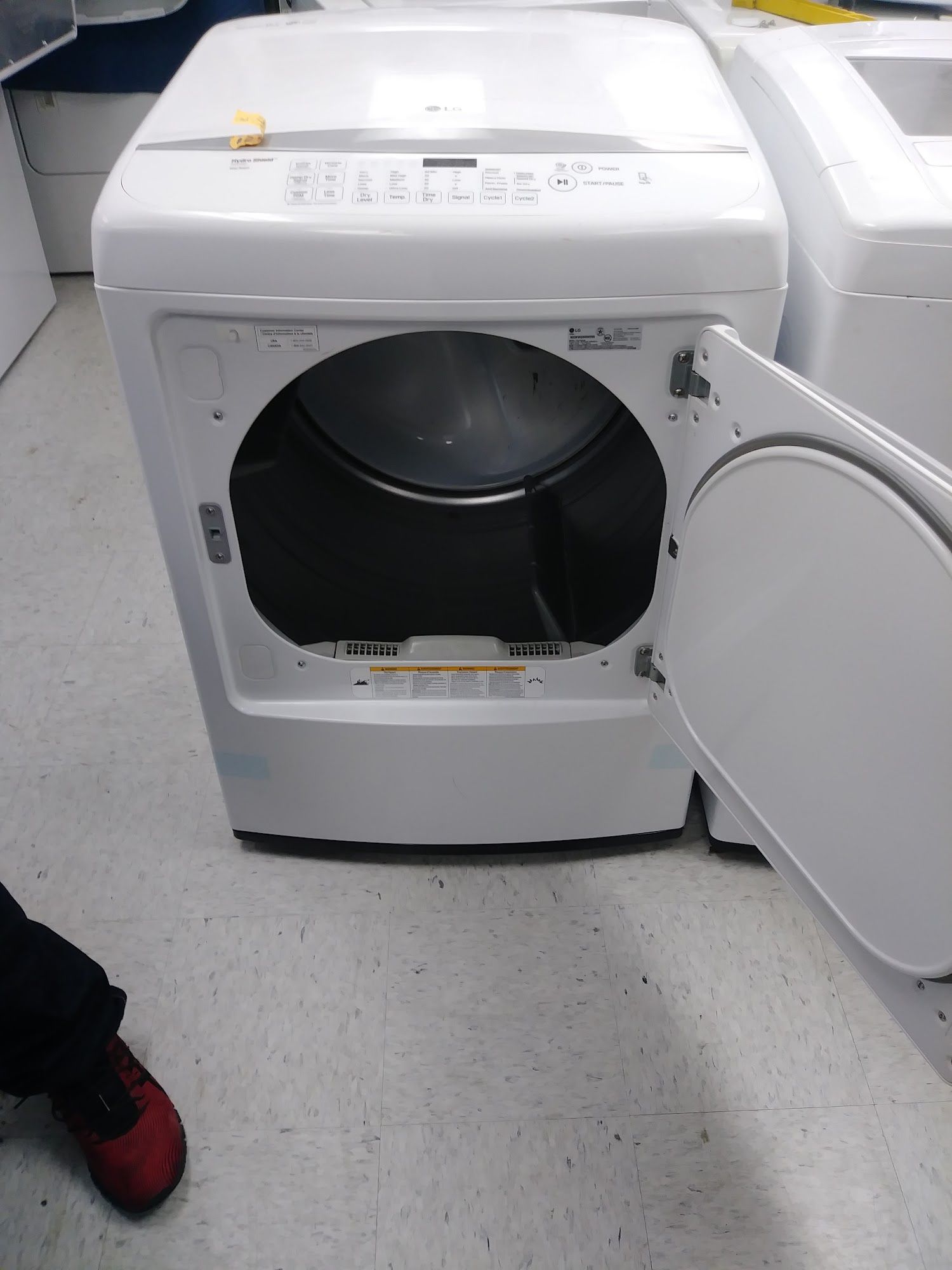 White dryer with open door; interior drum visible. Red shoe visible in the foreground.