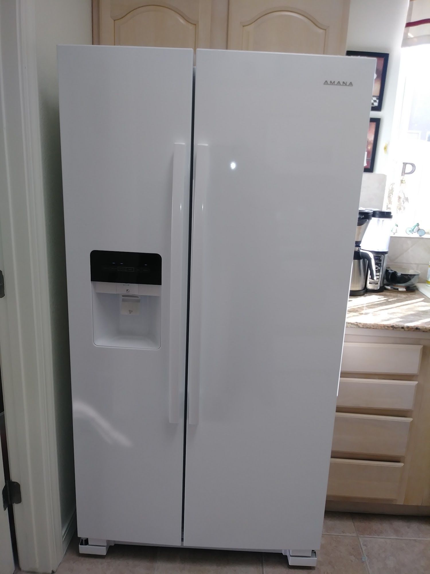 White Amana side-by-side refrigerator with water dispenser in a kitchen.
