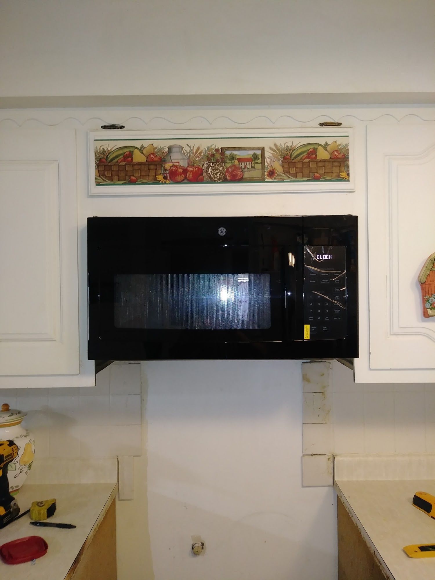 Black microwave installed in kitchen cabinet with artwork above it.