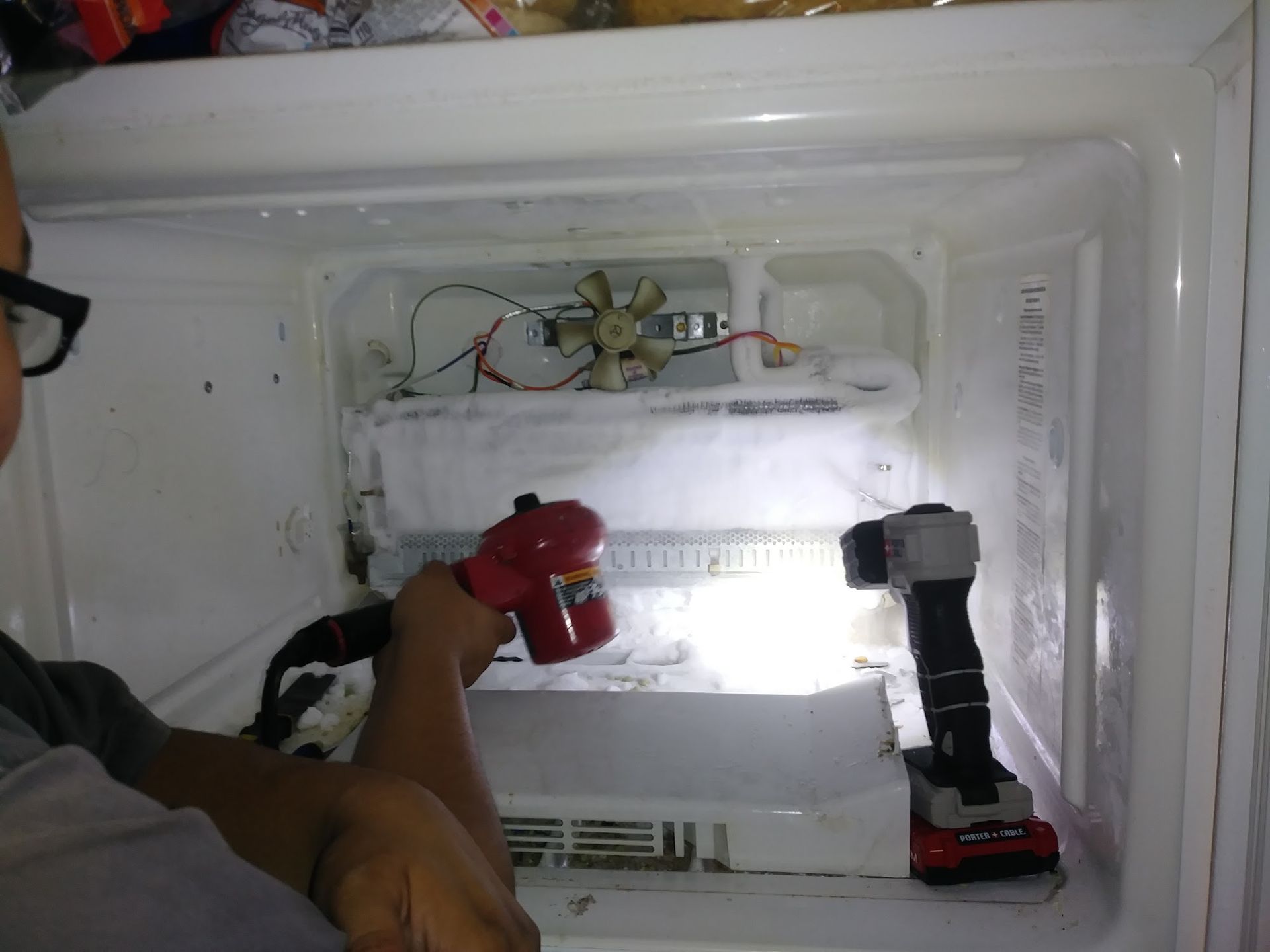 Person melting ice in a freezer with a heat gun and flashlight.