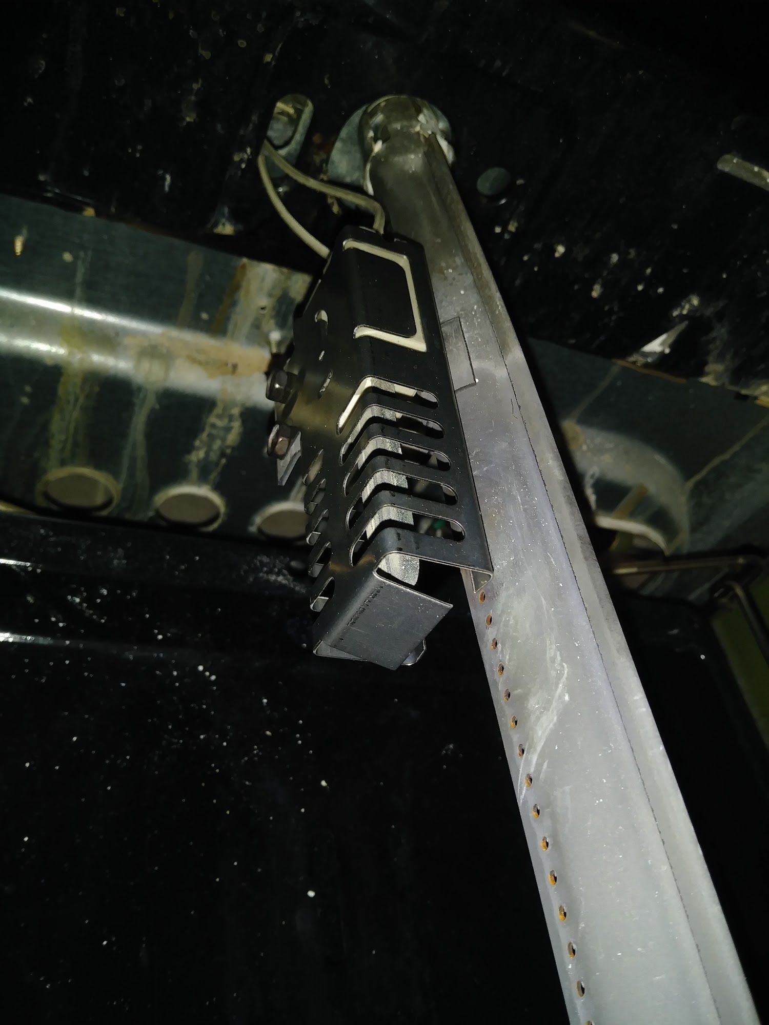 Metal structure with a black box attached to a long, metallic pole, likely inside a vehicle.