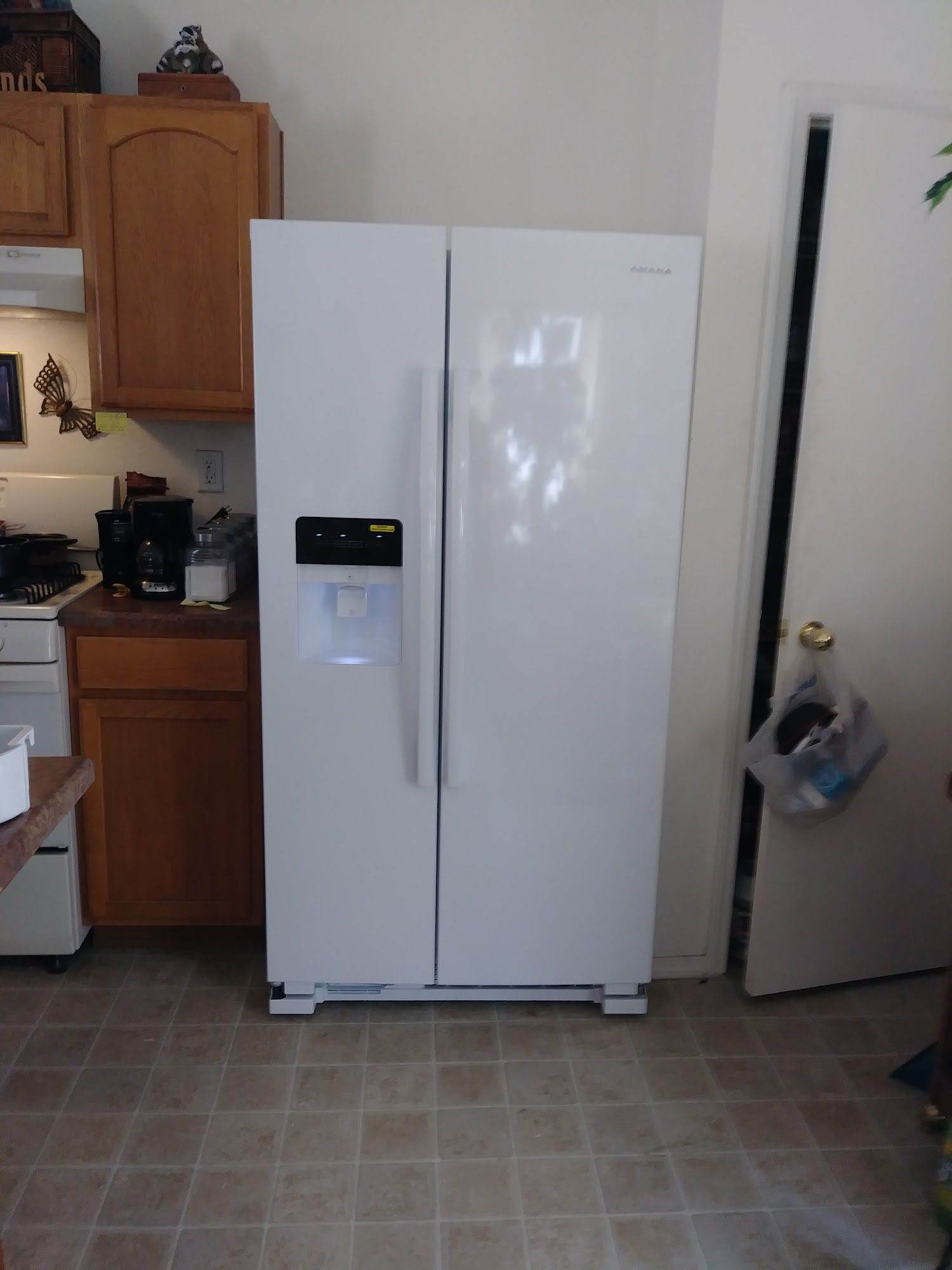 White side-by-side refrigerator in a kitchen next to a wooden cabinet and a door.