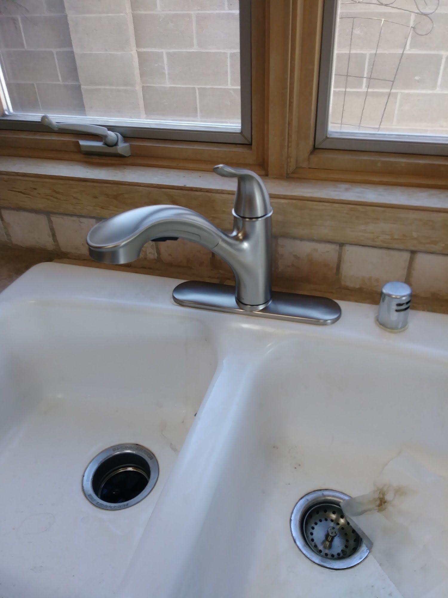 White double sink with a silver faucet, set in a kitchen with a window above.