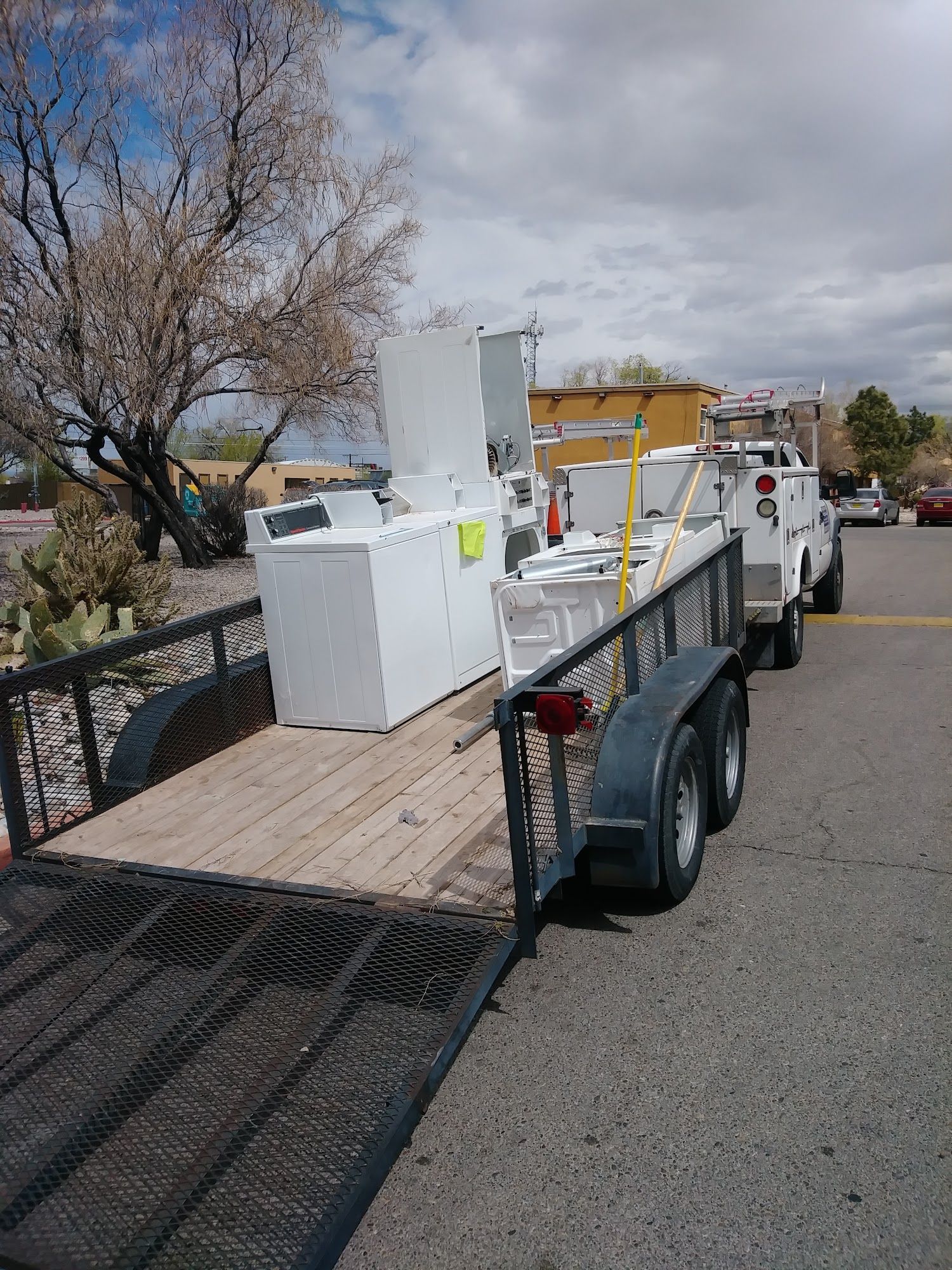 A trailer loaded with white appliances, pulled by a white truck, on a sunny day.