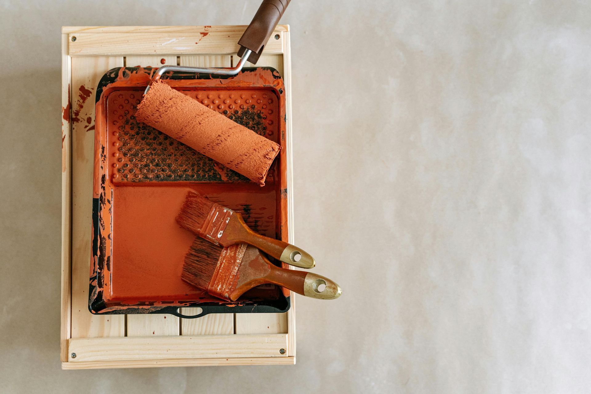 Paint supplies: Paint tray with orange paint, paint roller, and two paint brushes.