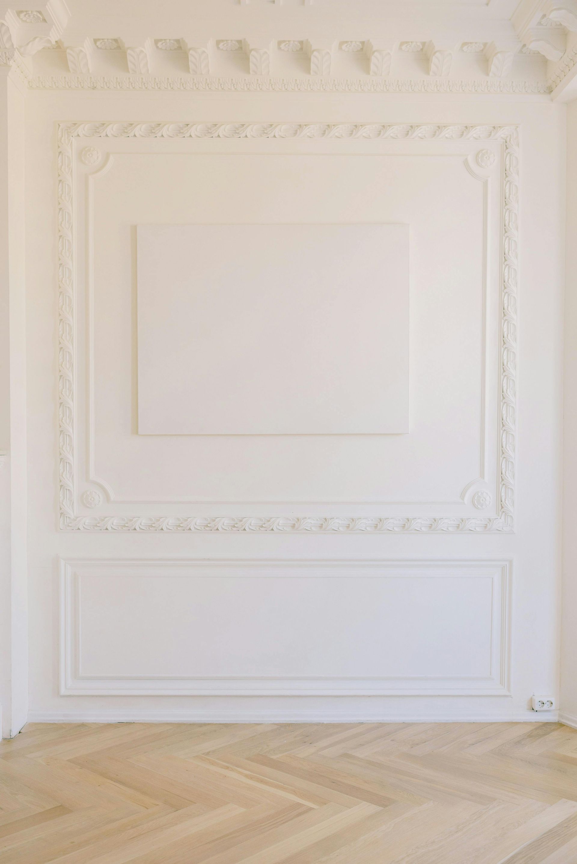 White room with ornate molding, blank canvas, and herringbone wood floor.