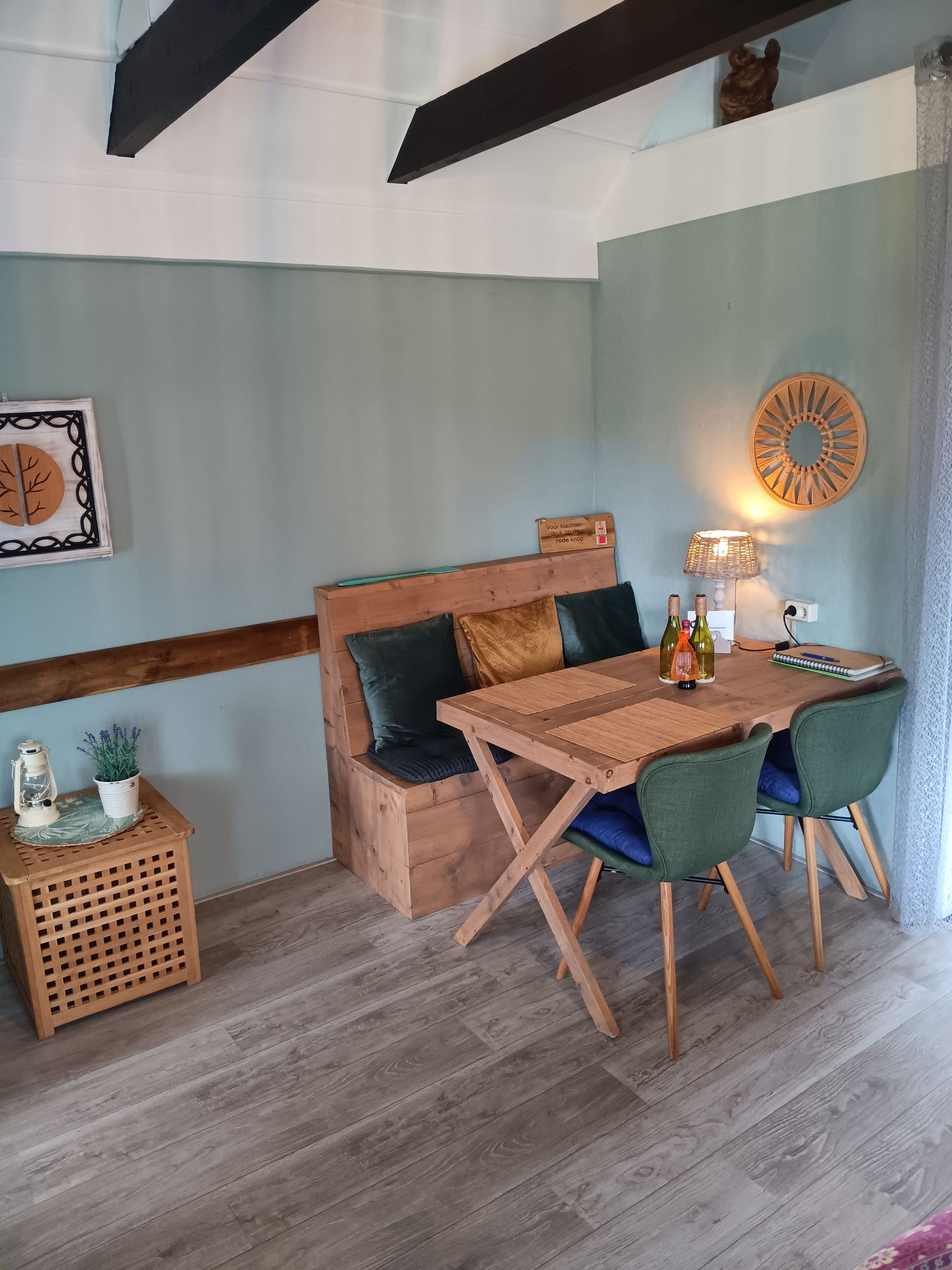 Gezellige eethoek met houten tafel, groene stoelen, zitbank, muurdecoratie en een brandende lamp onder een schuin plafond.