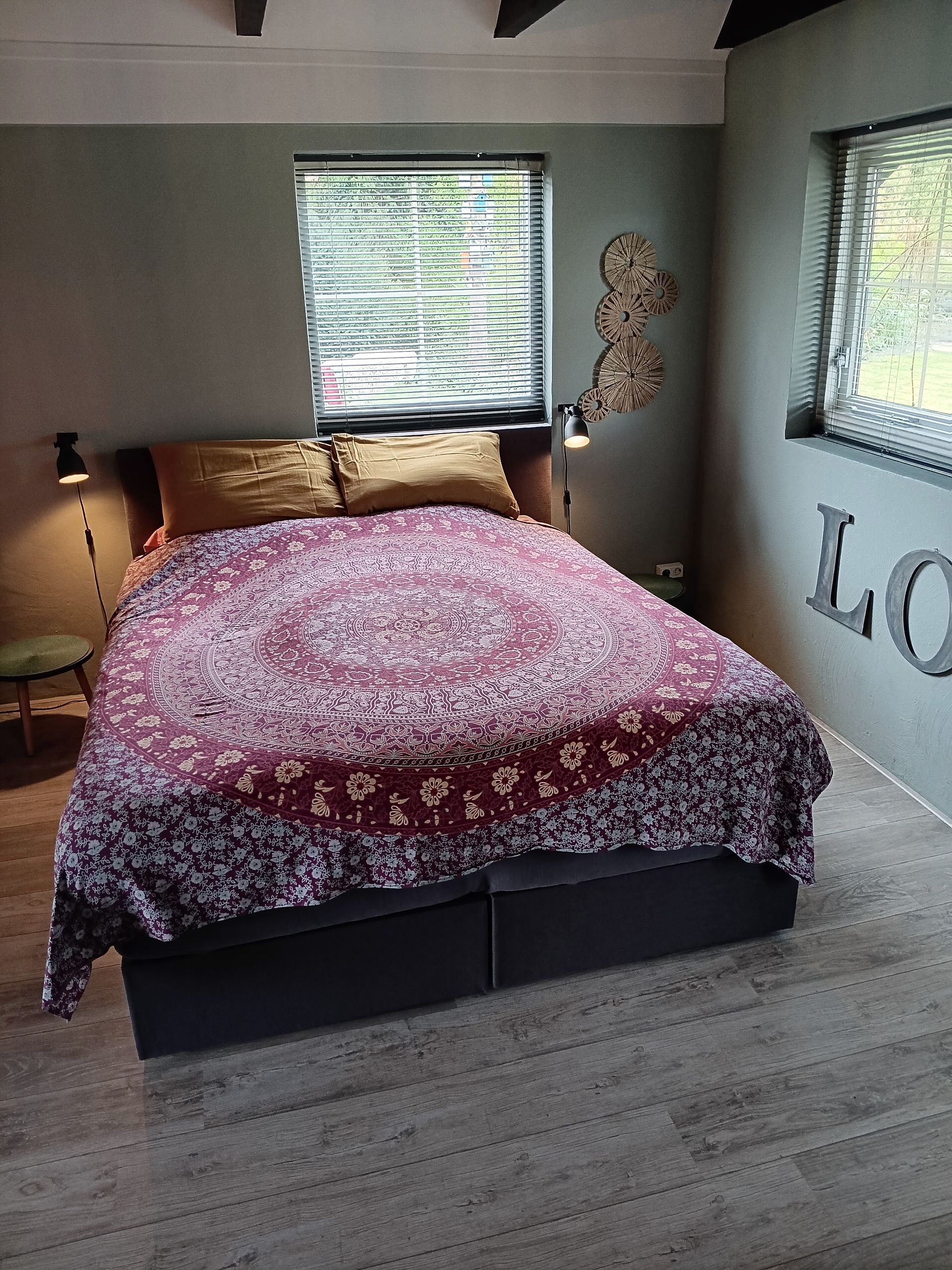 Gezellige slaapkamer met een rood patroon op de sprei, twee ramen, een warme lamp en 