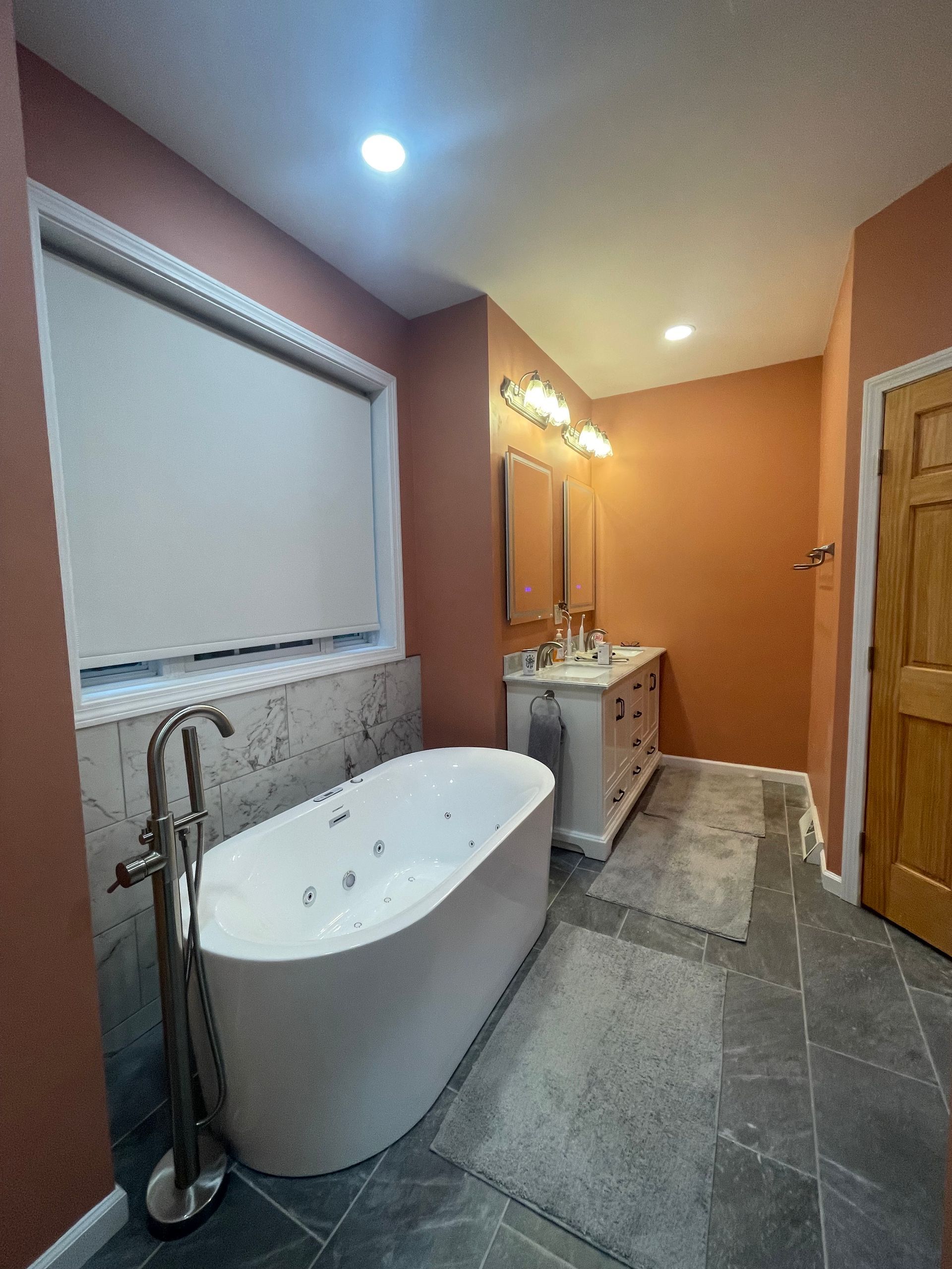 Bathroom with a white tub, vanity, and orange walls. Gray tile floor.