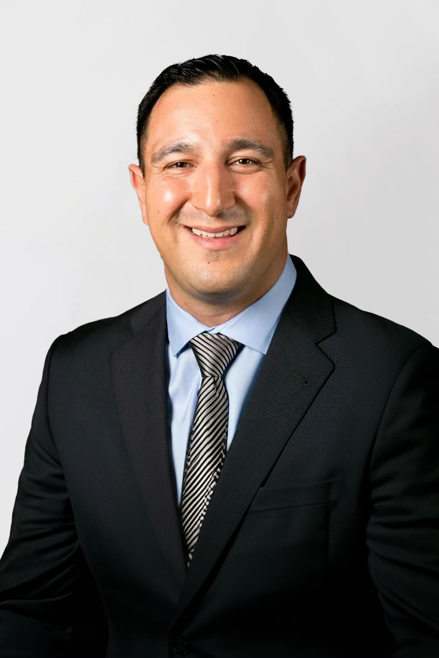 A man in a suit and vest is standing in front of a white background.