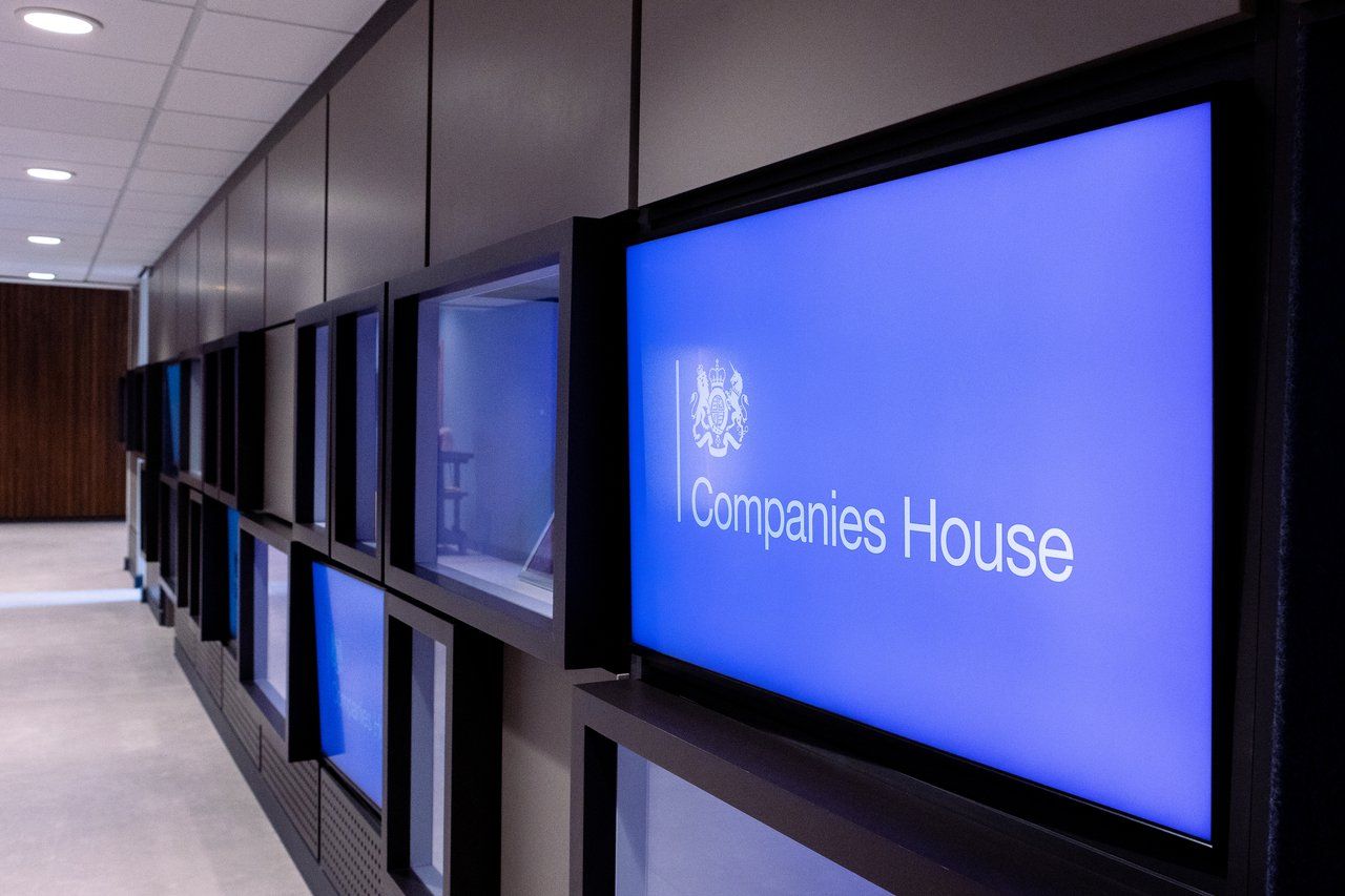 Hallway with Companies House logo on a blue screen; other screens and wood paneling on the wall.