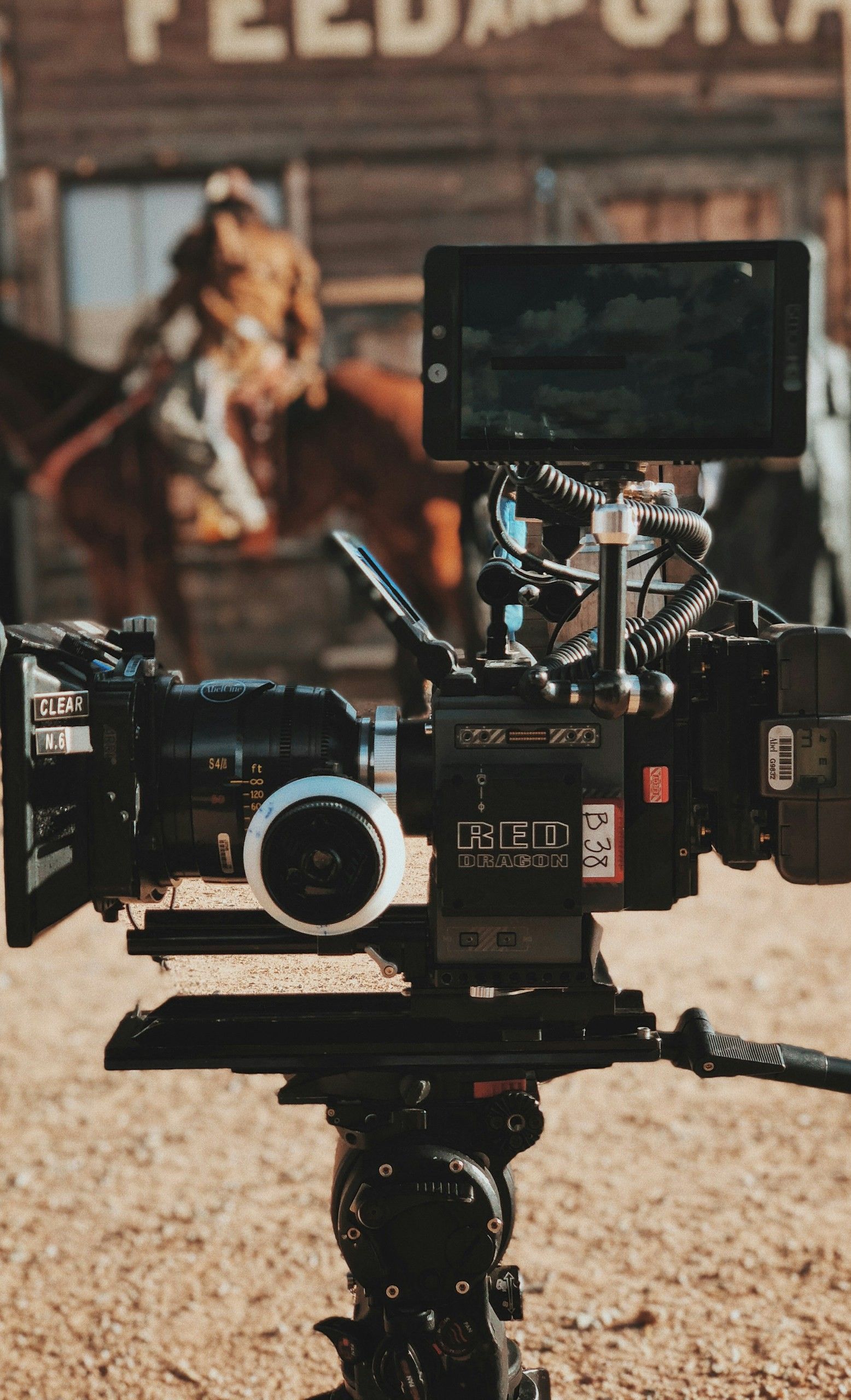 Film camera on tripod with horse in background, filming on a movie set.