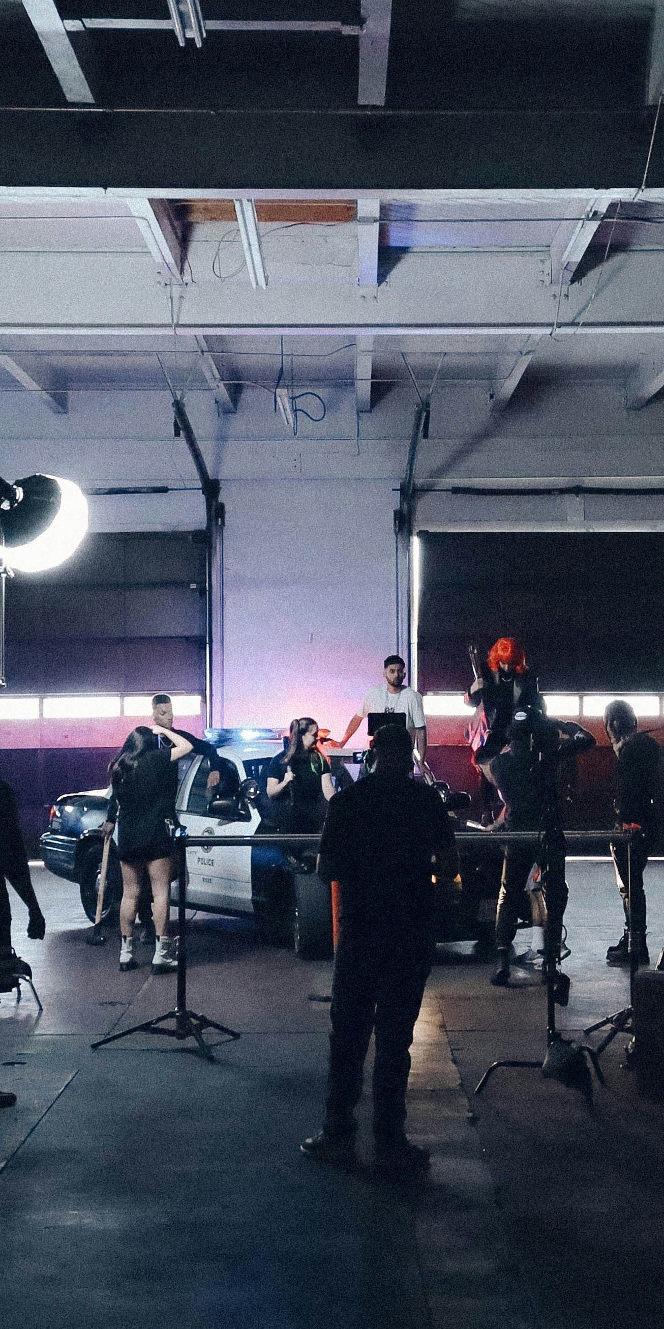 A police car is in a garage with a film crew present, filming a scene.