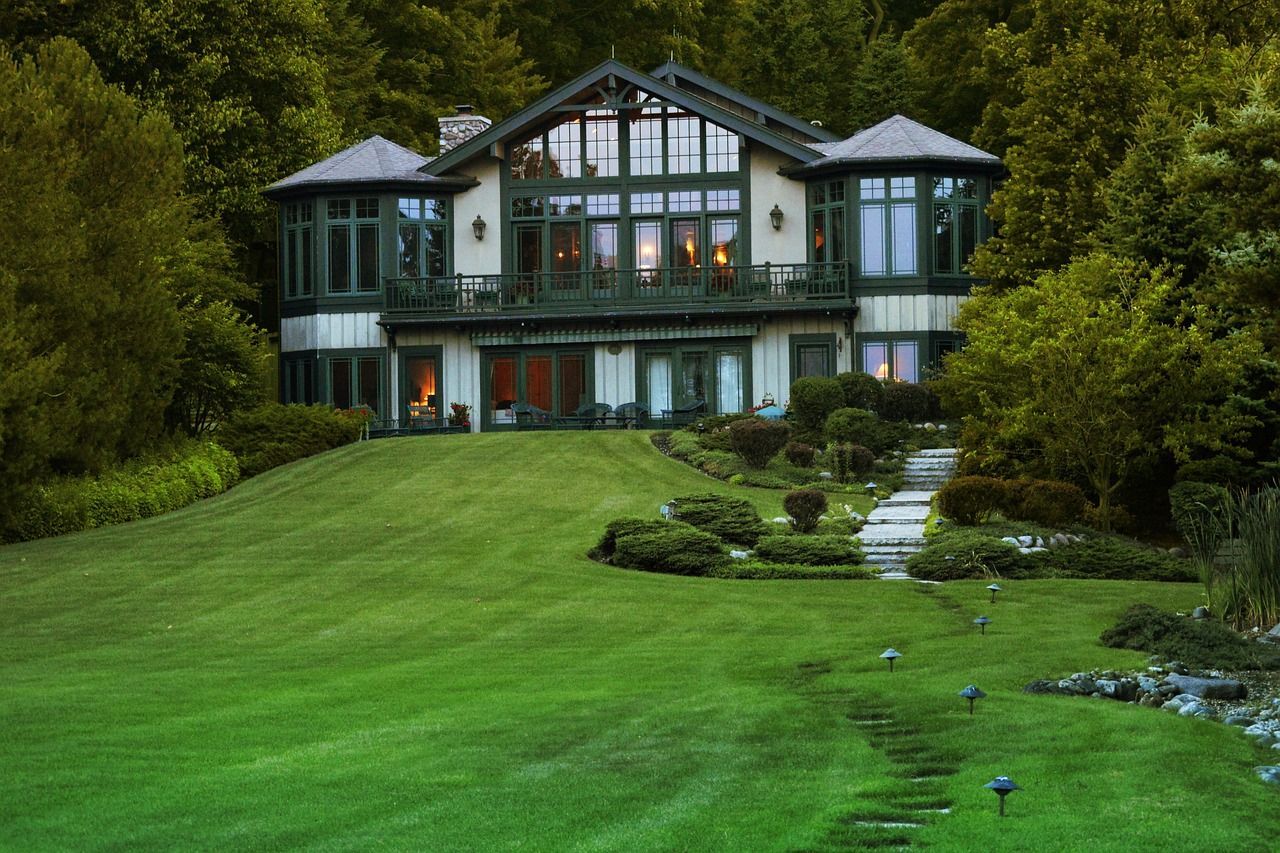 A large house is sitting on top of a lush green hill surrounded by trees.