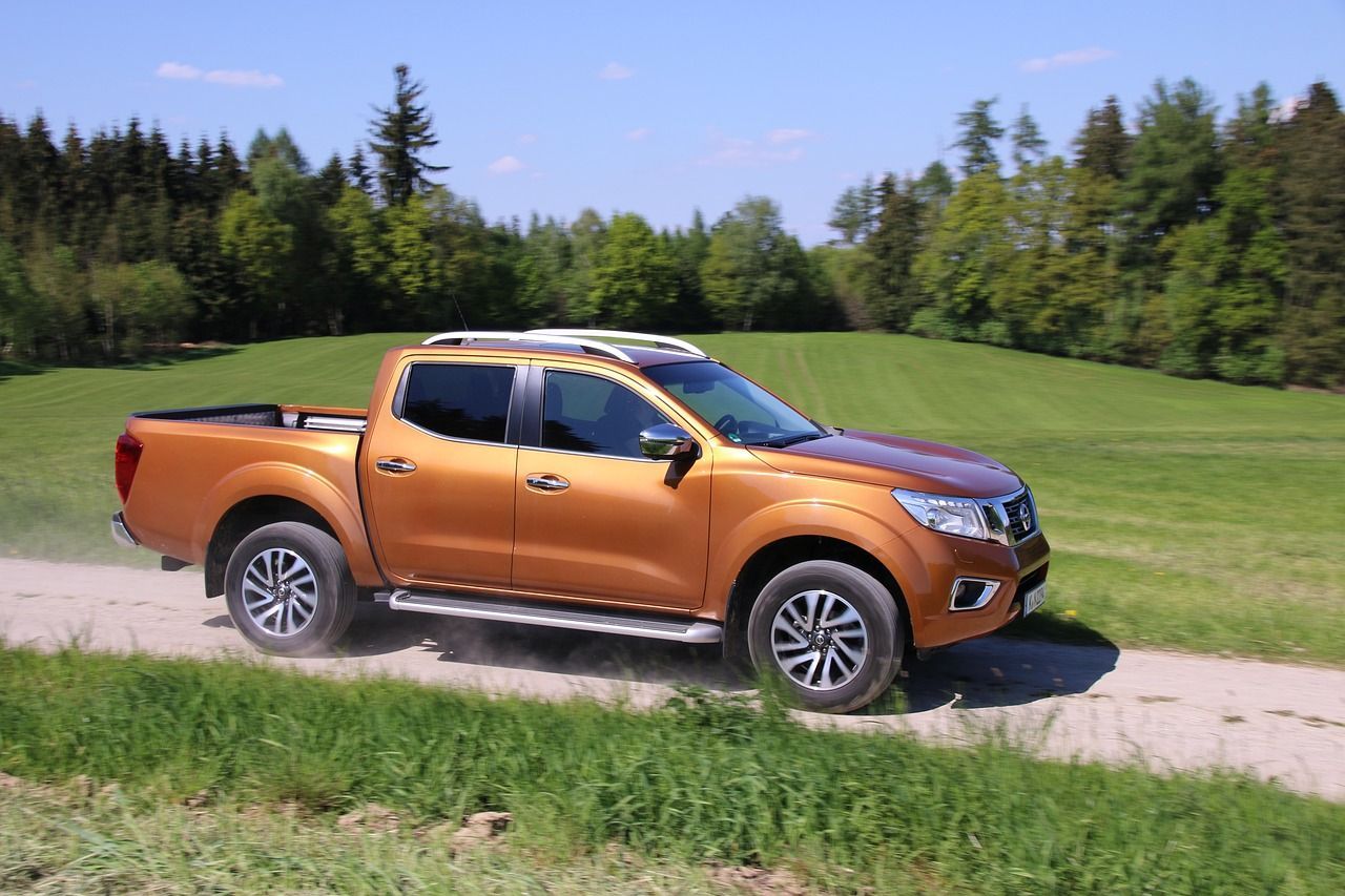 A pickup truck is driving down a dirt road next to a field.