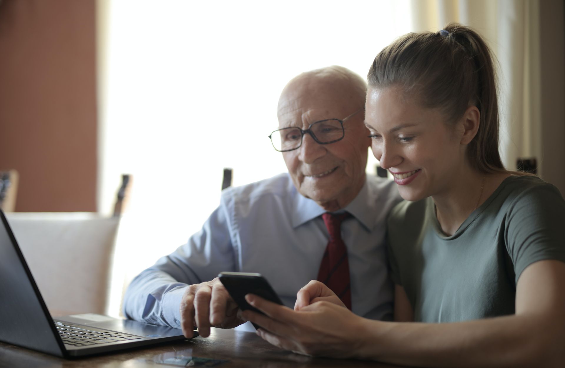 Grandfather in suit sat with his adult granddaughter in front of laptop
