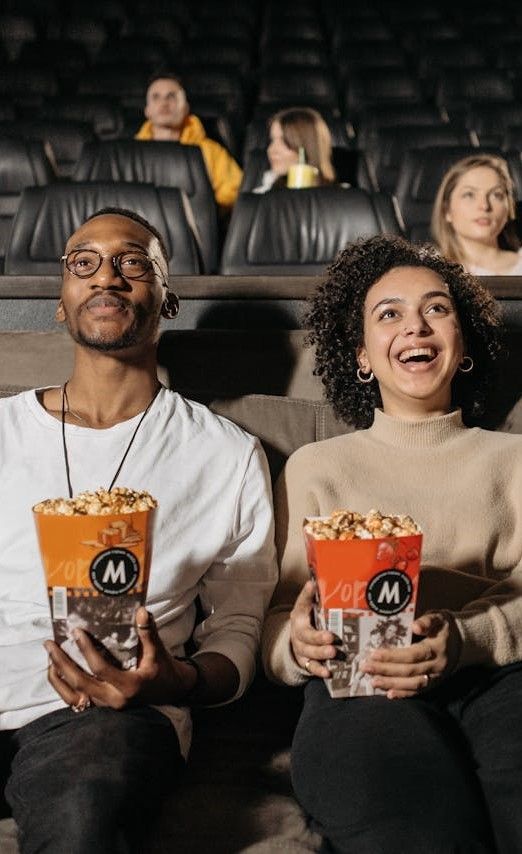 A man and a woman are sitting in a theatre holding buckets of popcorn.