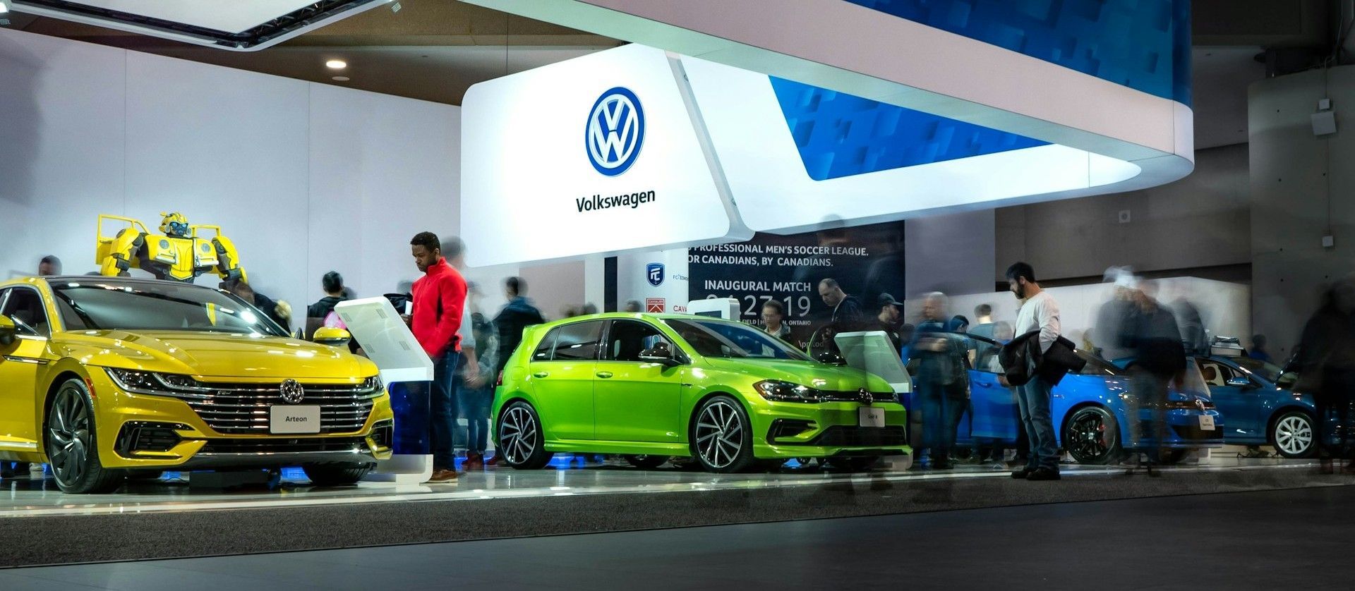 Volkswagen display with yellow and green cars and people viewing them at an auto show