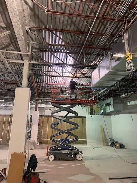 Un homme se tient debout sur une nacelle à ciseaux et travaille sur le plafond d'un immeuble.