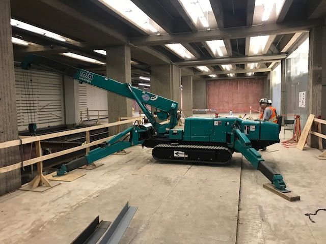 Un homme conduit une grue verte dans un immeuble en construction.