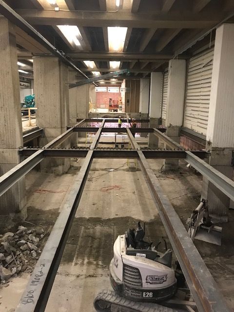 Une petite excavatrice est posée sur une poutre métallique dans un bâtiment en construction.