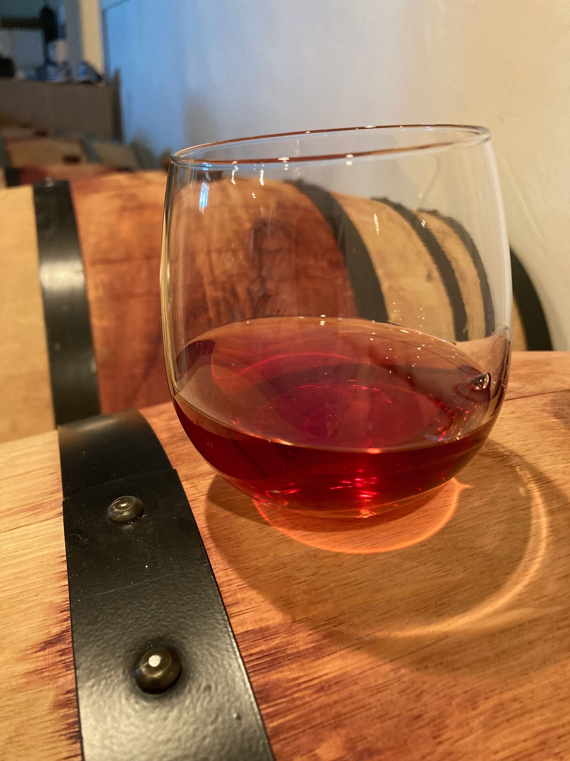 A glass of wine sits on top of a barrel