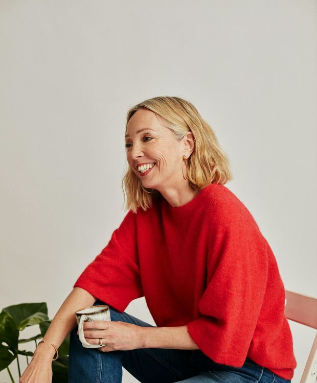 A woman in a red sweater is sitting on a chair holding a cup of coffee.