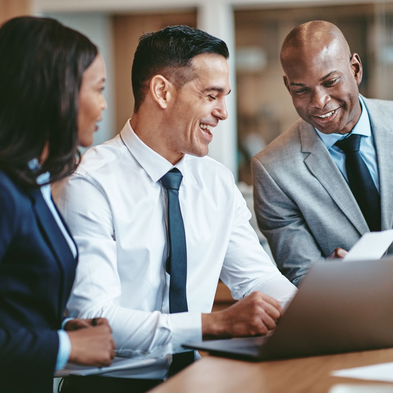 A group of business people are sitting around a table looking at a laptop computer.