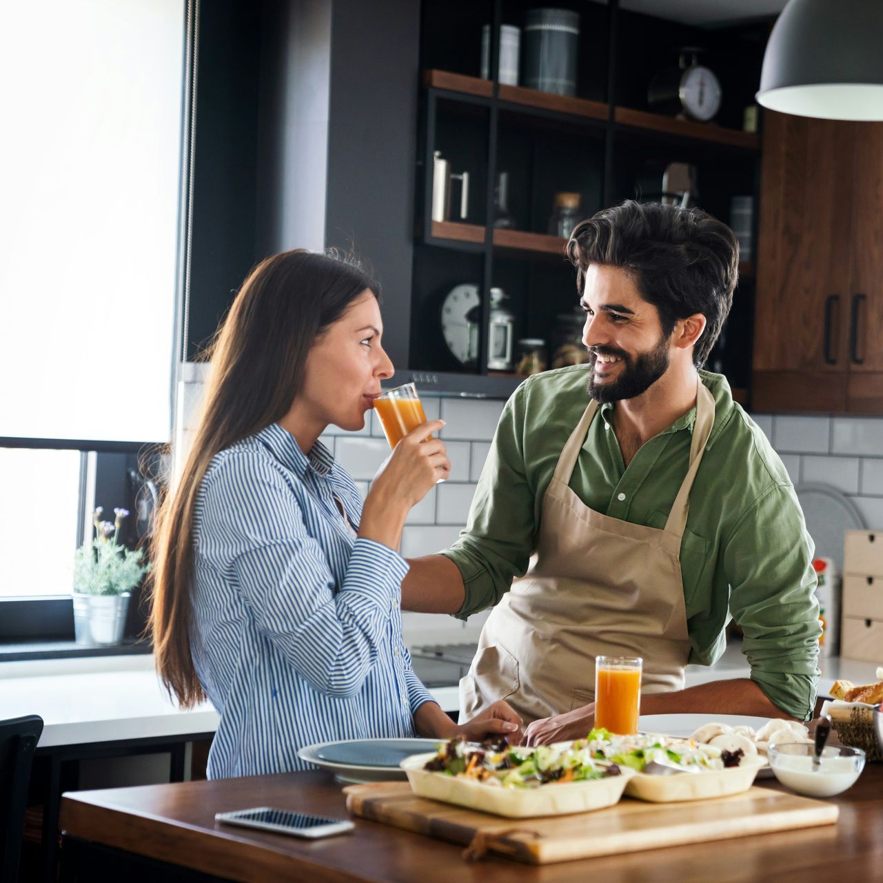 A man and a woman are sitting at a table in a kitchen drinking orange juice.