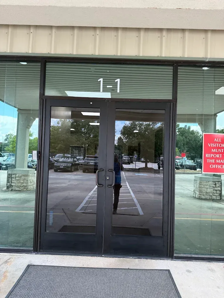 Double glass doors labeled 1-1 at a building entrance with a visitor sign and parking lot reflection.