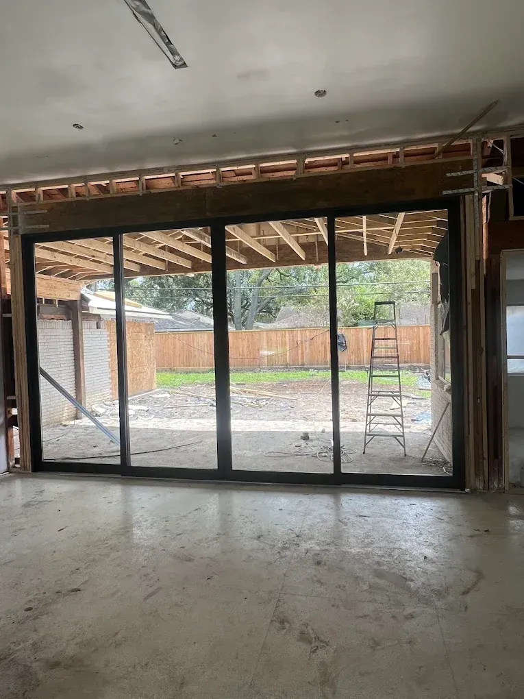A wide black sliding glass door installed in a room under construction, overlooking a backyard with a wooden fence.