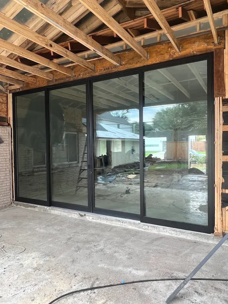 A large, four-panel black sliding glass door installed in an unfinished house frame, looking out toward a yard.