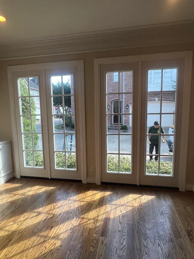 Two sets of white French doors looking out onto a brick building and a person standing outside on a sunny day.
