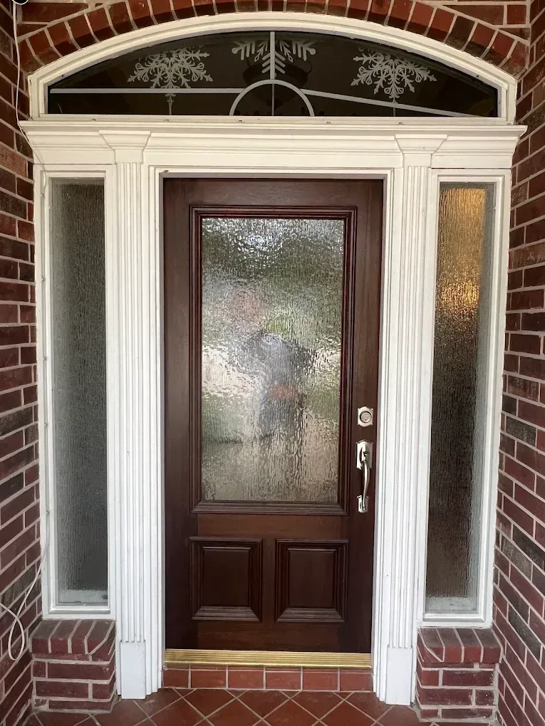 Dark wooden front door with a glass panel, flanked by narrow frosted windows, under a white frame with arched transom.