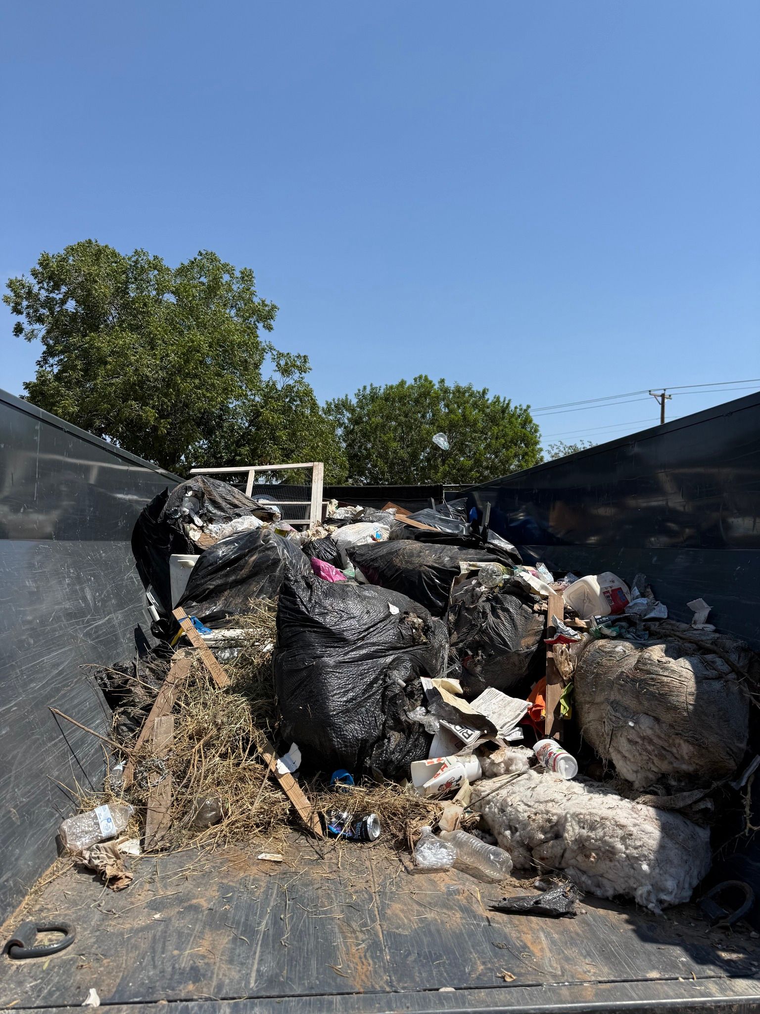 Dumpster filled with trash bags and debris under a clear blue sky.